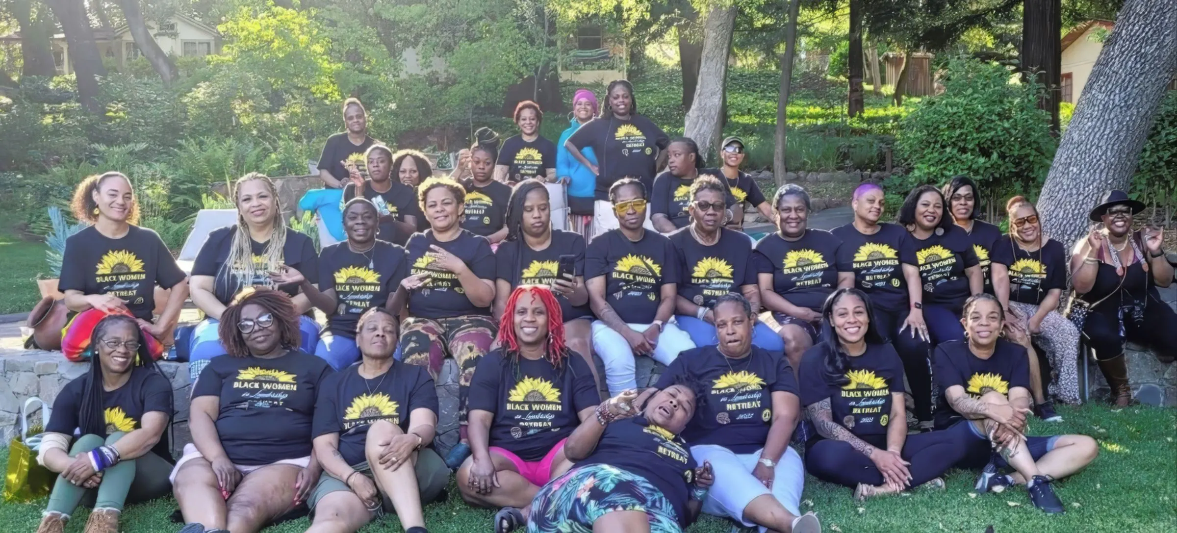 Women in Black Women in Leadership shirts sitting together on a lawn at the 2022 retreat